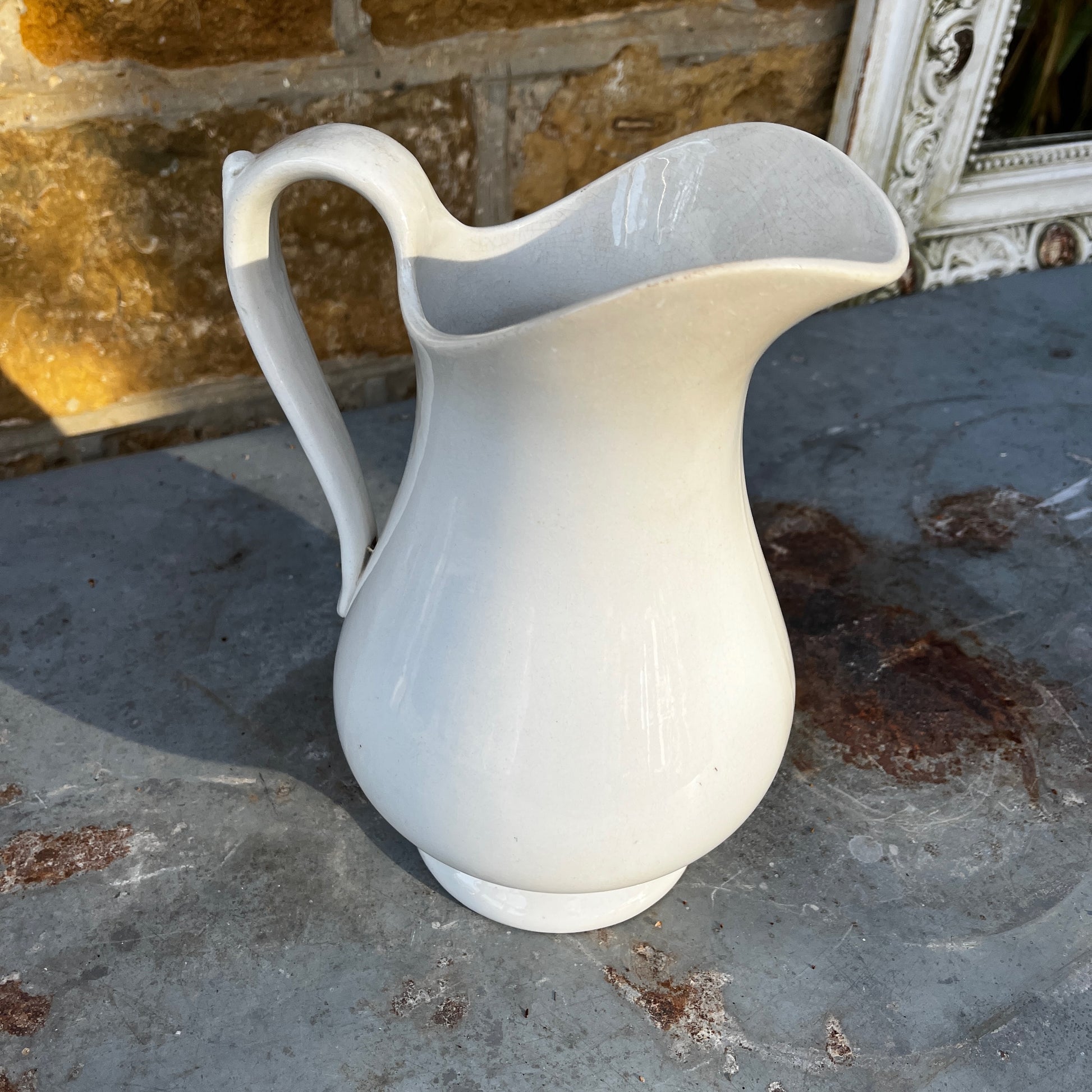 Simple French white ceramic jug with a elongated scalloped body, curved handle, and minimalist glazed finish in a classic utilitarian style.