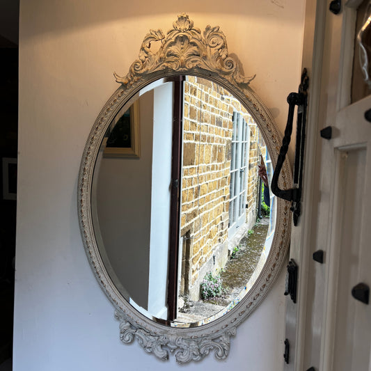 Large vintage French oval bevelled mirror painted white, featuring decorative detailing at the top and bottom with an elegant aged finish.
