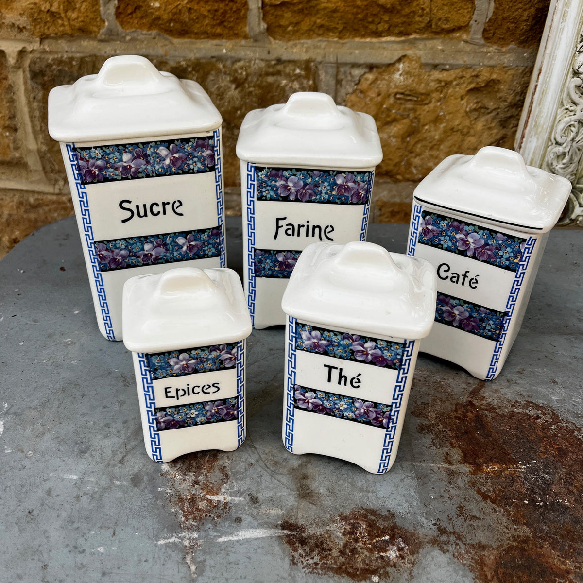 Five ceramic kitchen canisters arranged together, each decorated with a floral transfer print and French lettering on a vintage Czechoslovakian design