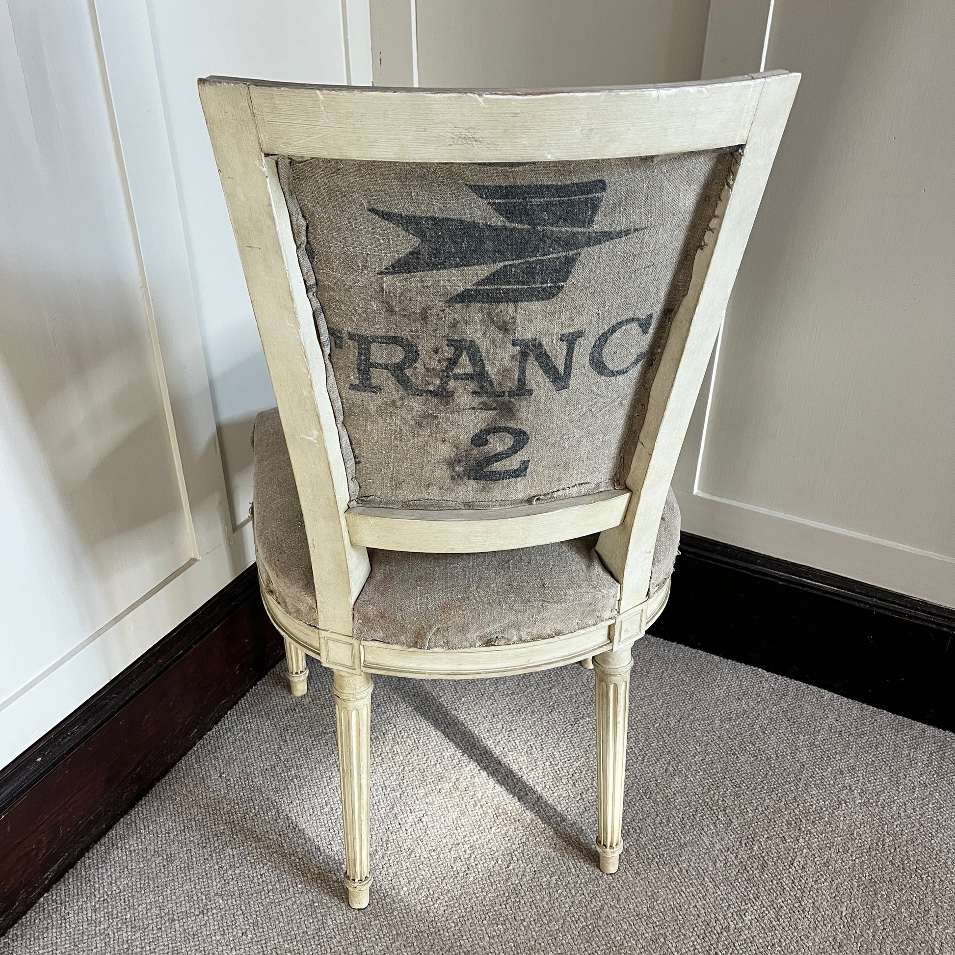 A French chair with a semi-upholstered design, featuring a wooden frame painted in a distressed finish and a back & seat covered in La Poste fabric with its iconic grey and black postal pattern. The chair combines rustic elegance with vintage charm