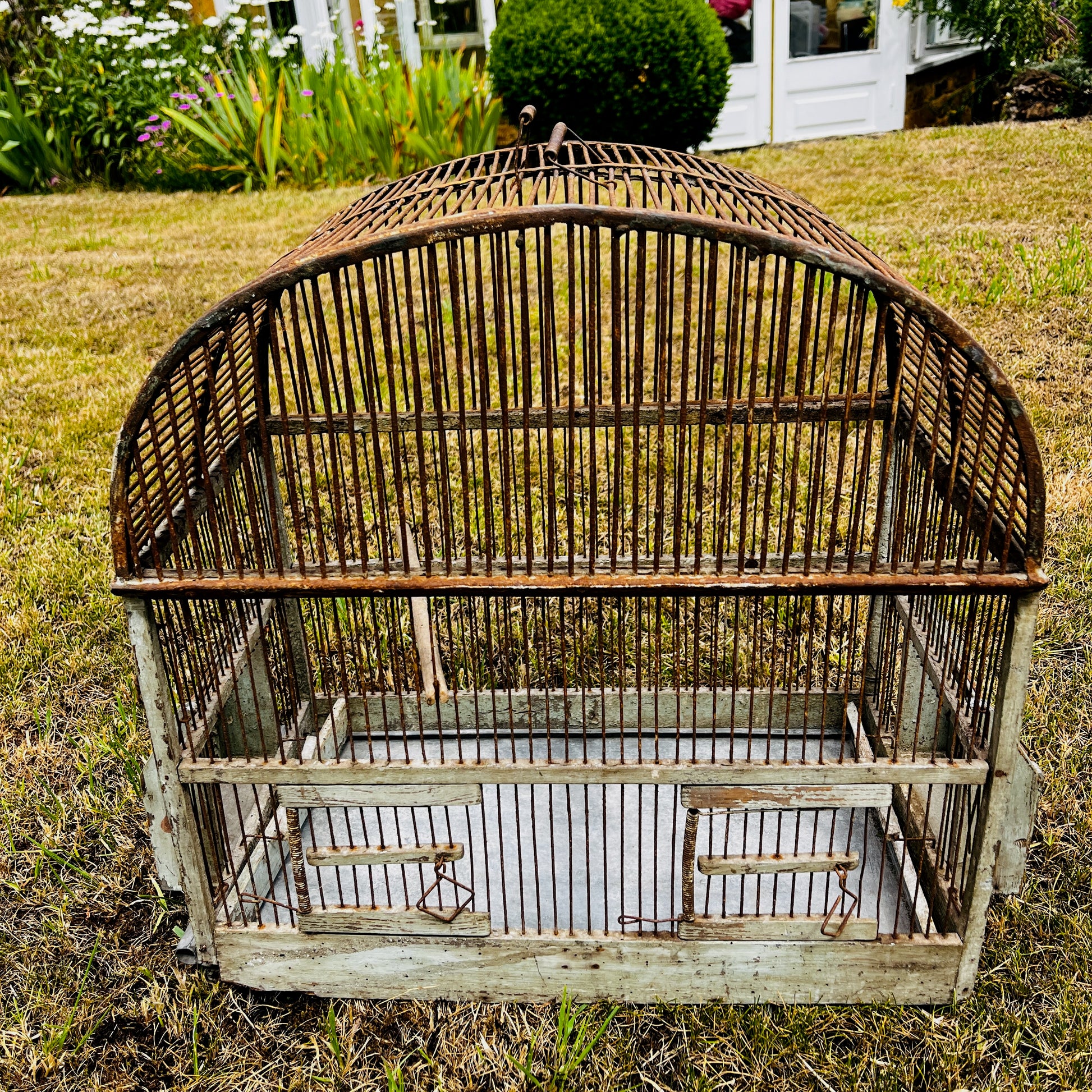 Large vintage birdcage with an ornate metal frame, featuring a domed top, decorative detailing, and a weathered aged finish.