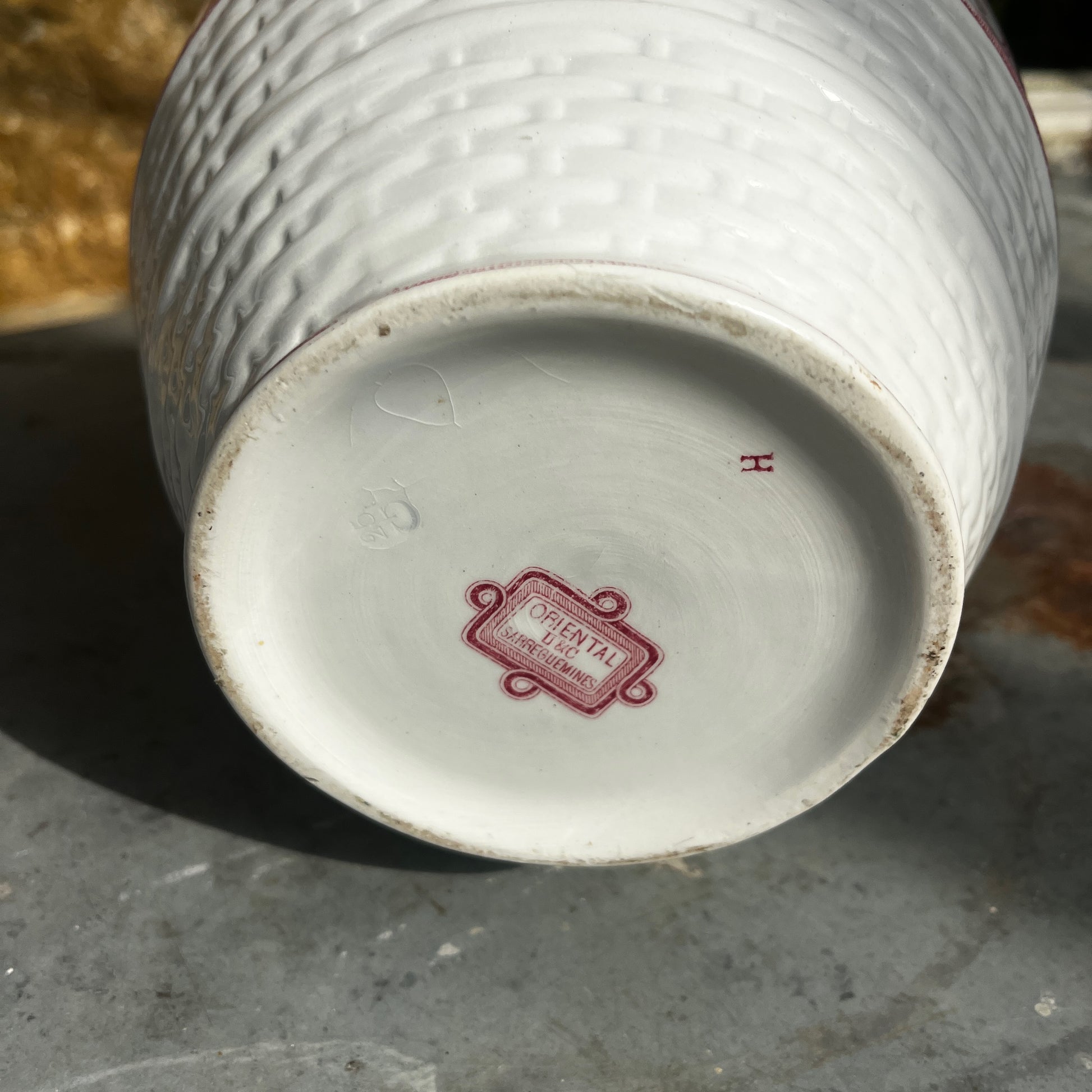 An antique French Sarreguemines ironstone pitcher featuring a classic pink transferware floral pattern on a creamy white background. The generously sized pitcher has a curved handle, gently flared rim, and elegant rounded form, with subtle signs of age and wear that enhance its vintage character.
