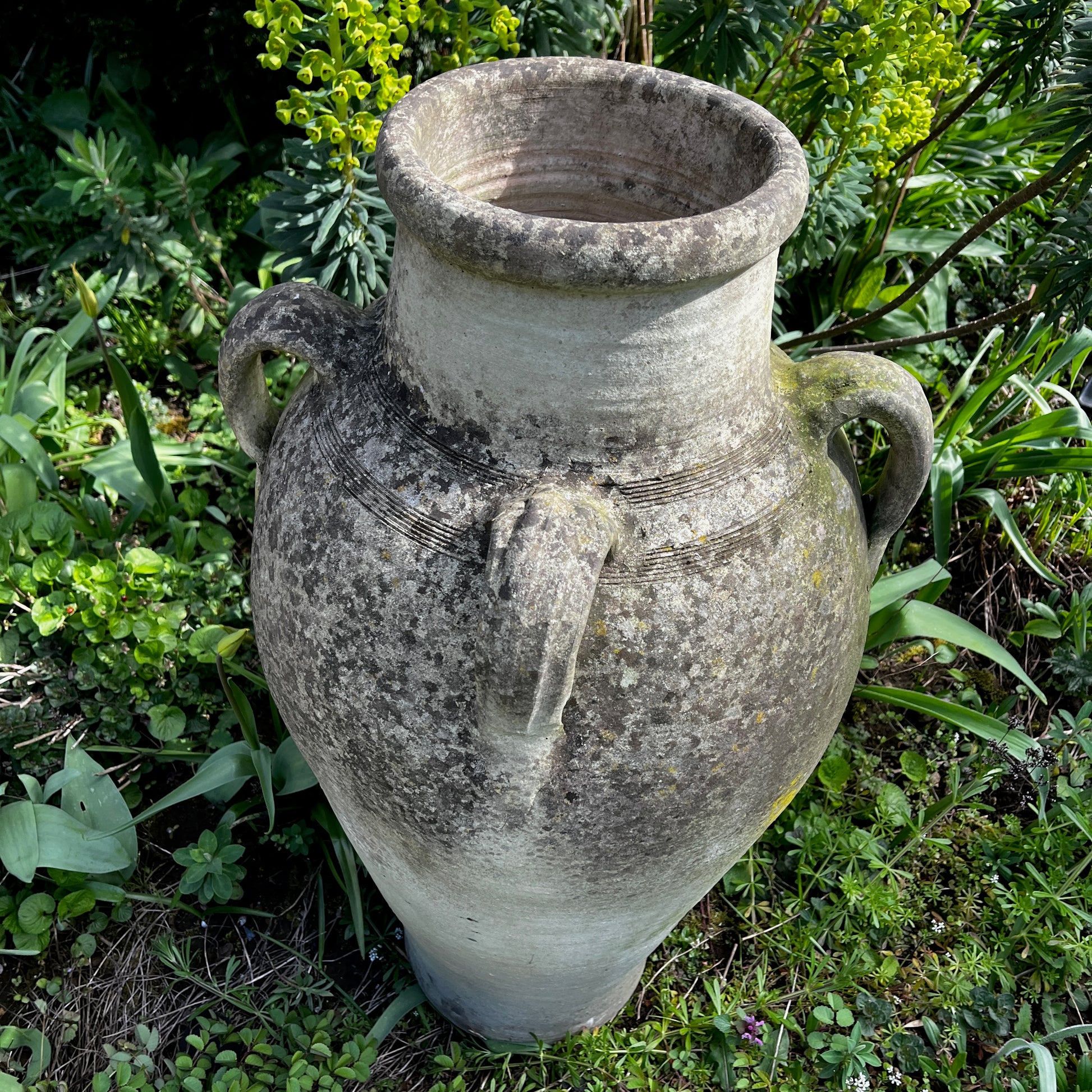 Large rustic garden urn with an aged weathered surface and traces of green lichen, featuring a classic decorative shape and timeworn outdoor character.