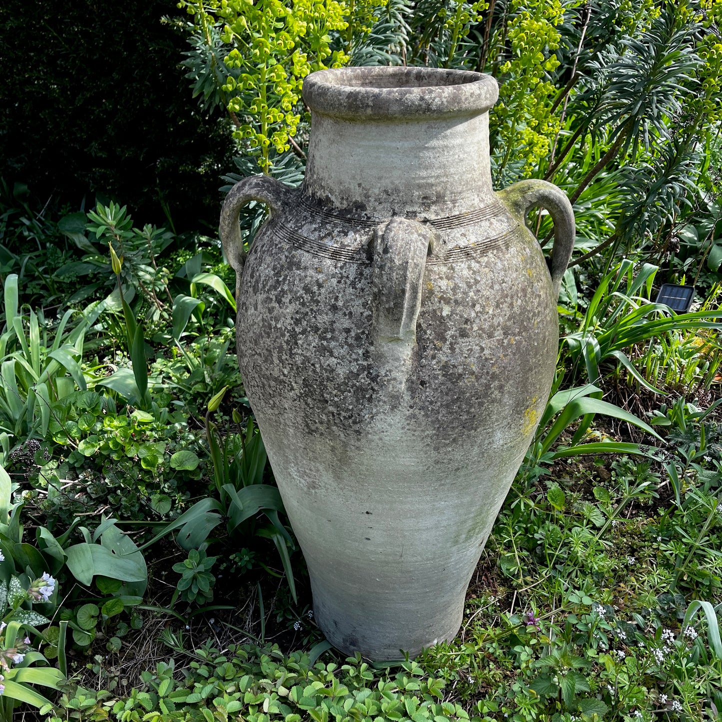 Large rustic garden urn with an aged weathered surface and traces of green lichen, featuring a classic decorative shape and timeworn outdoor character.