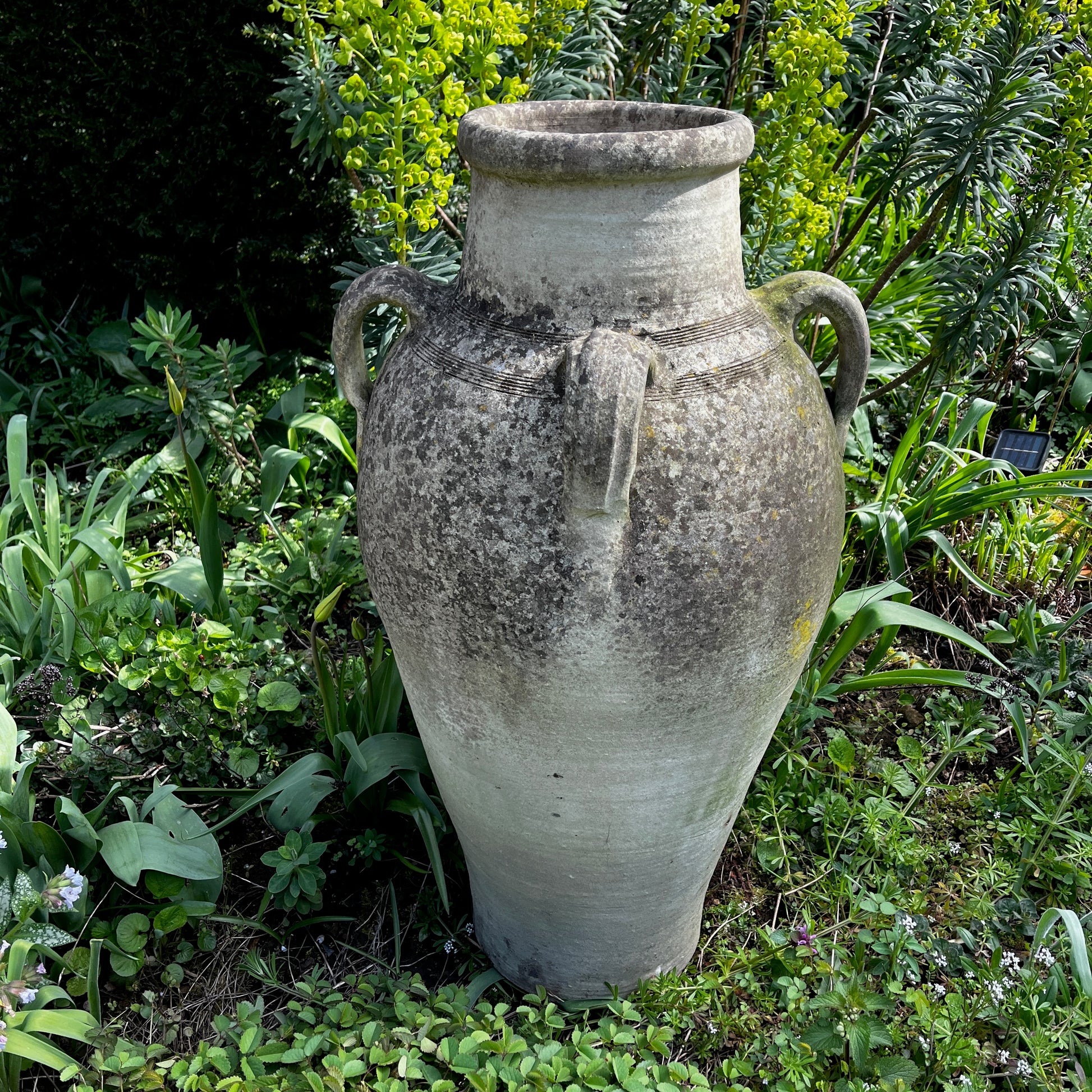 Large rustic garden urn with an aged weathered surface and traces of green lichen, featuring a classic decorative shape and timeworn outdoor character.