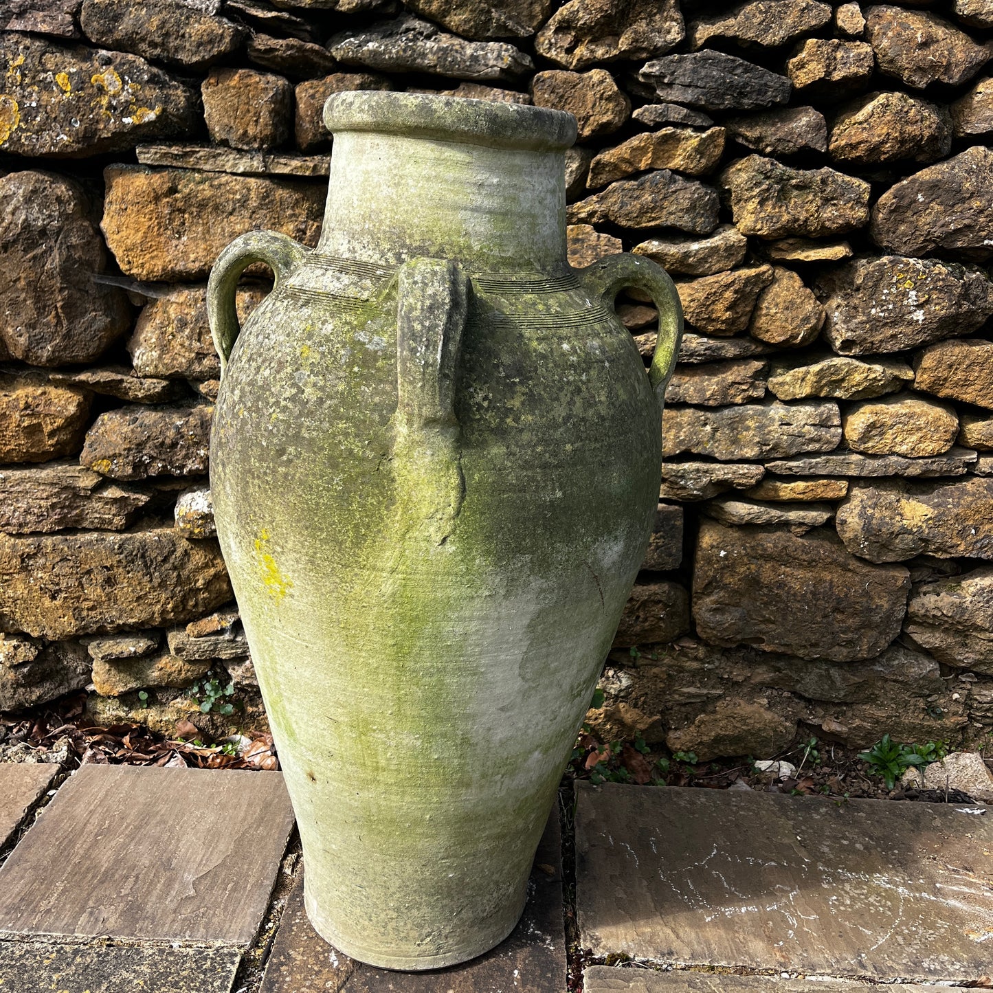 Large rustic garden urn with an aged weathered surface and traces of green lichen, featuring a classic decorative shape and timeworn outdoor character.