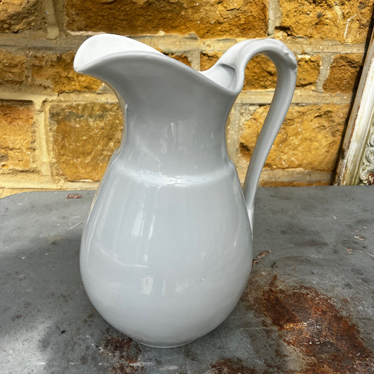 A large vintage white ironstone jug featuring a classic rounded form, wide opening, and an ornate decorative handle. The jug has a softly aged white glazed finish with subtle signs of wear that enhance its timeless character.
