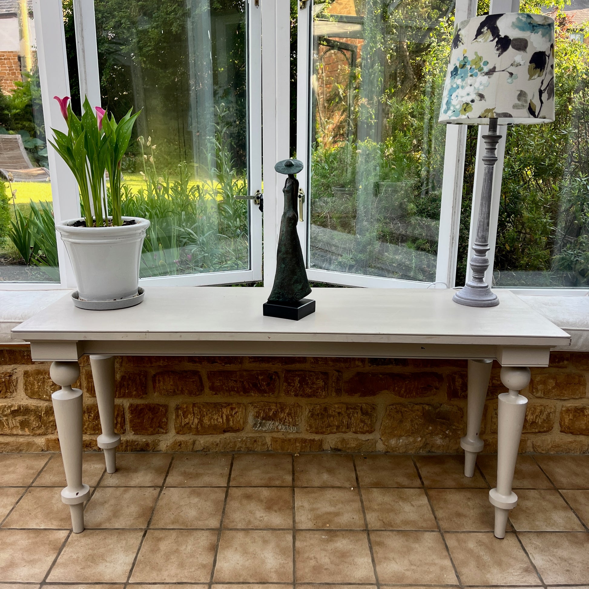 A long grey vintage console table with a weathered finish, featuring a sleek rectangular top and small drawers at each end. The table stands on decorative legs, exuding elegance