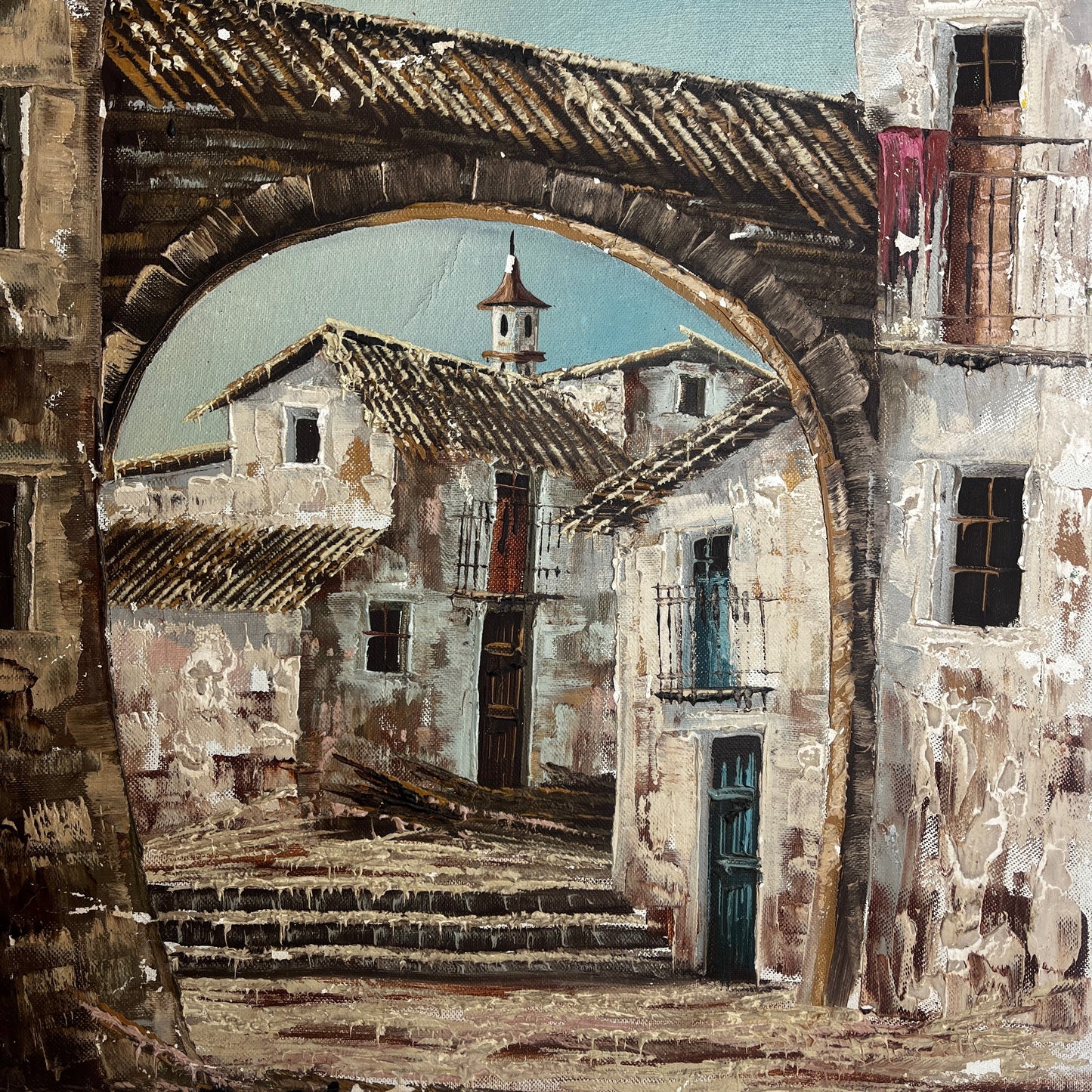 An oil painting depicting a rustic French village scene viewed through a large stone archway, with weathered buildings, tiled roofs, and a pale blue sky.