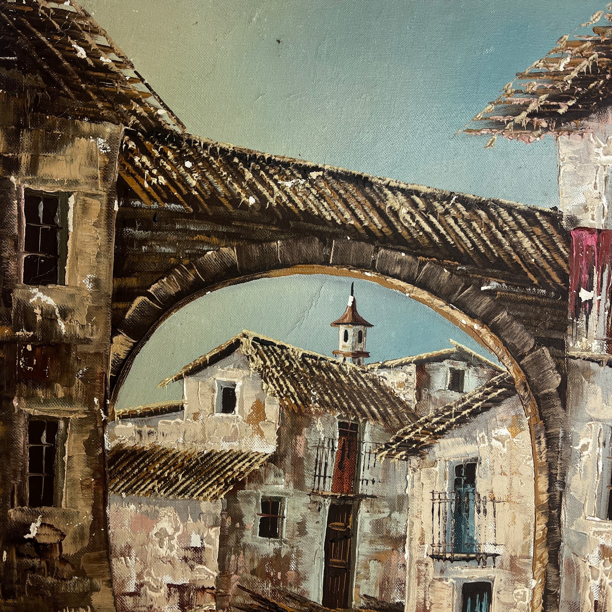 An oil painting depicting a rustic French village scene viewed through a large stone archway, with weathered buildings, tiled roofs, and a pale blue sky.