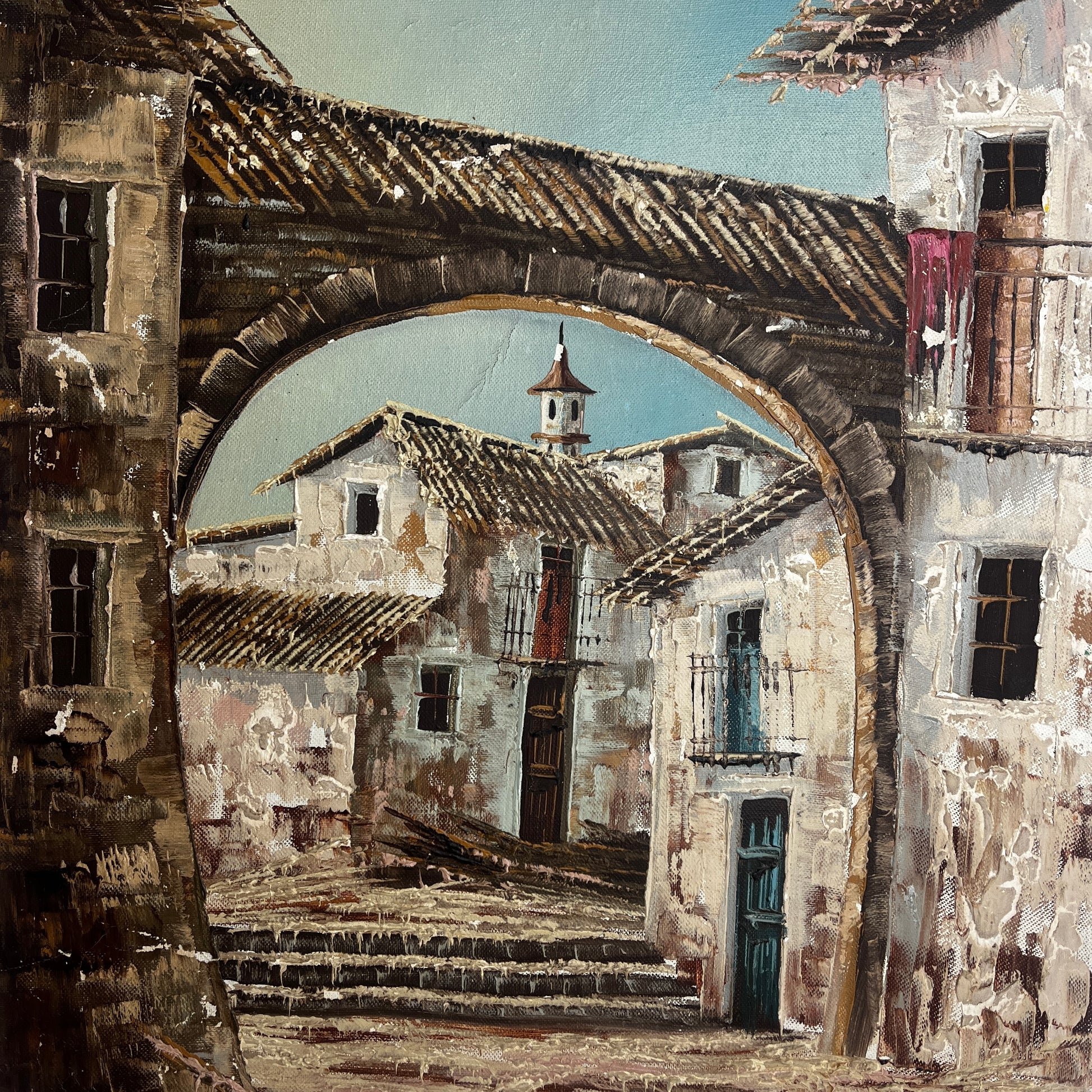 An oil painting depicting a rustic French village scene viewed through a large stone archway, with weathered buildings, tiled roofs, and a pale blue sky.