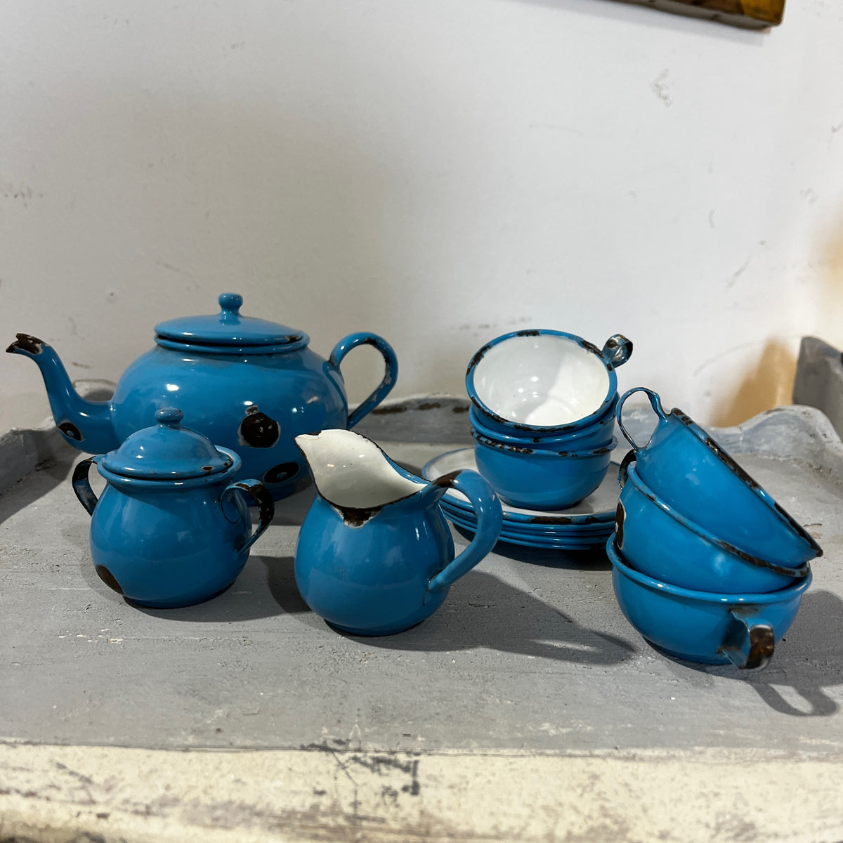 A vintage blue enamel tea set with a teapot, small pots, cups, and a pitcher, displayed on a gray surface.