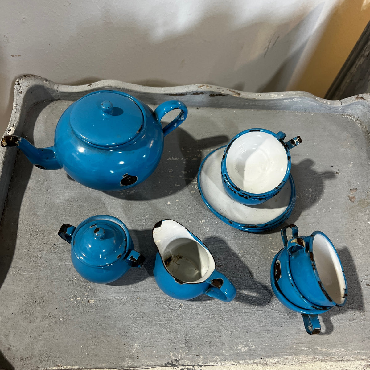 A vintage blue enamel tea set with a teapot, small pots, cups, and a pitcher, displayed on a gray surface.