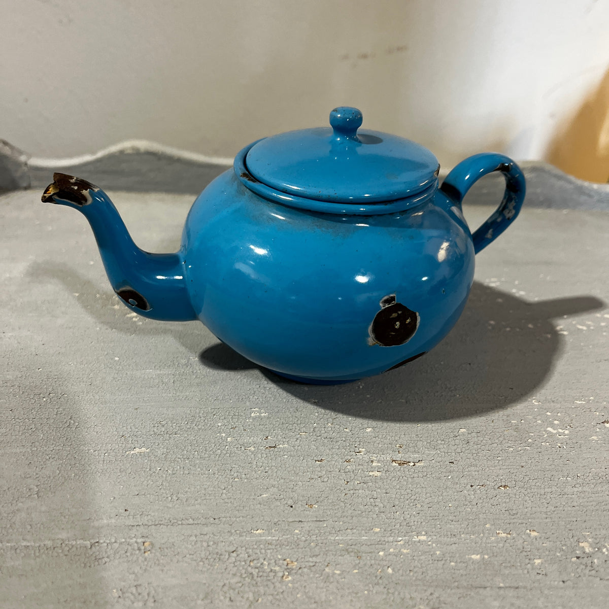 A vintage blue enamel tea set with a teapot, small pots, cups, and a pitcher, displayed on a gray surface.