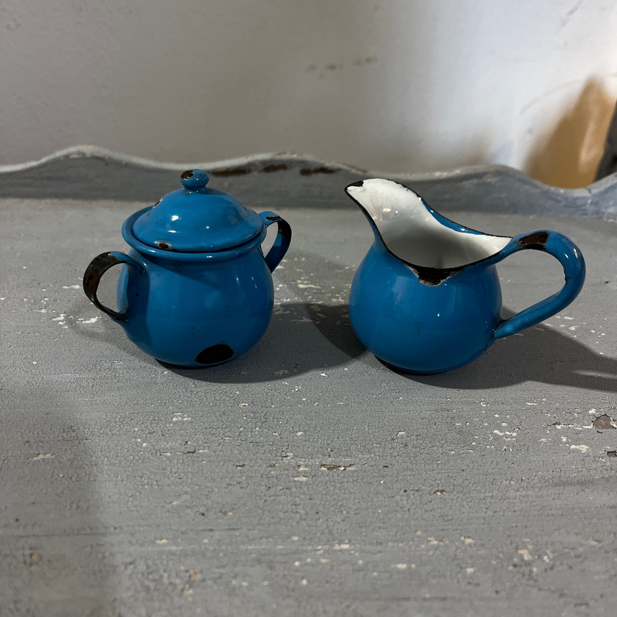 A vintage blue enamel tea set with a teapot, small pots, cups, and a pitcher, displayed on a gray surface.