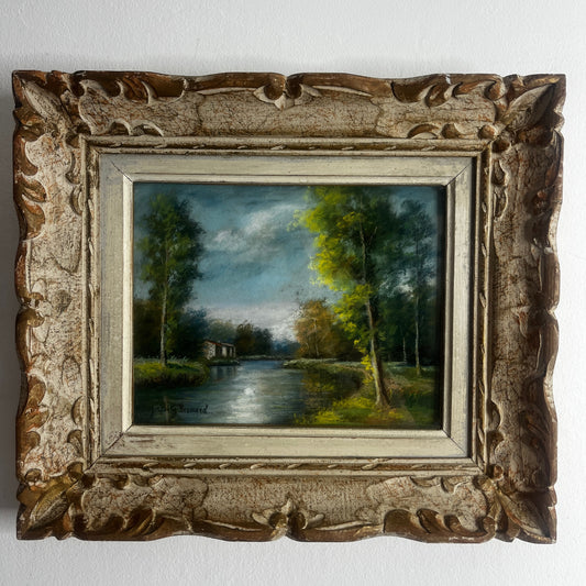 A vintage oil painting of a tranquil wooded landscape featuring a calm river or lake reflecting the sky, with trees lining the water and a small building nestled among the trees in the distance.  Montparnasse Frame.