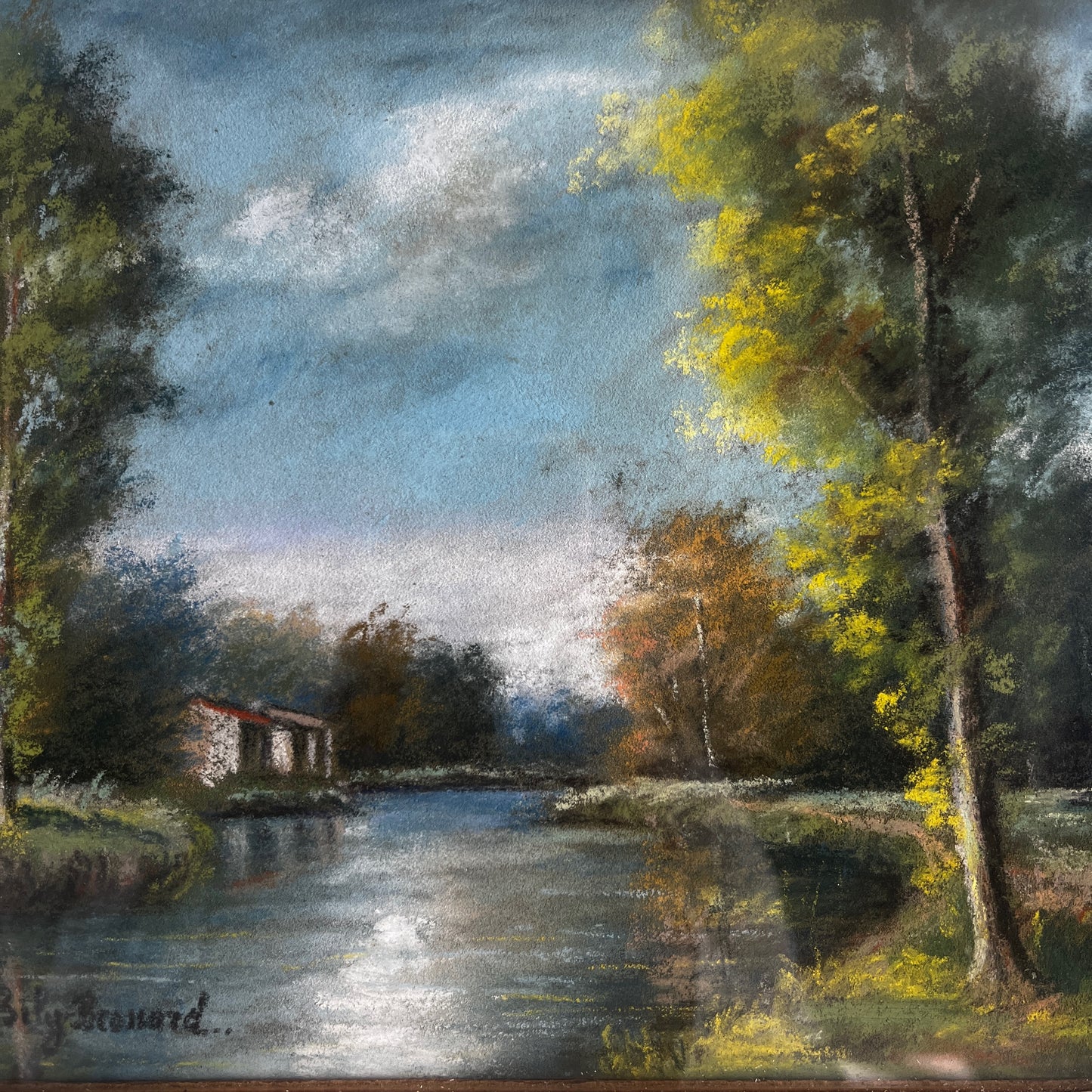 A vintage oil painting of a tranquil wooded landscape featuring a calm river or lake reflecting the sky, with trees lining the water and a small building nestled among the trees in the distance.  Montparnasse Frame.