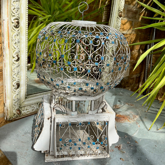 A Moroccan-style bird cage painted in blue and white, featuring intricate geometric and arabesque patterns. The cage has a domed top with a small finial, crafted from lightweight metal with open latticework, exuding exotic charm