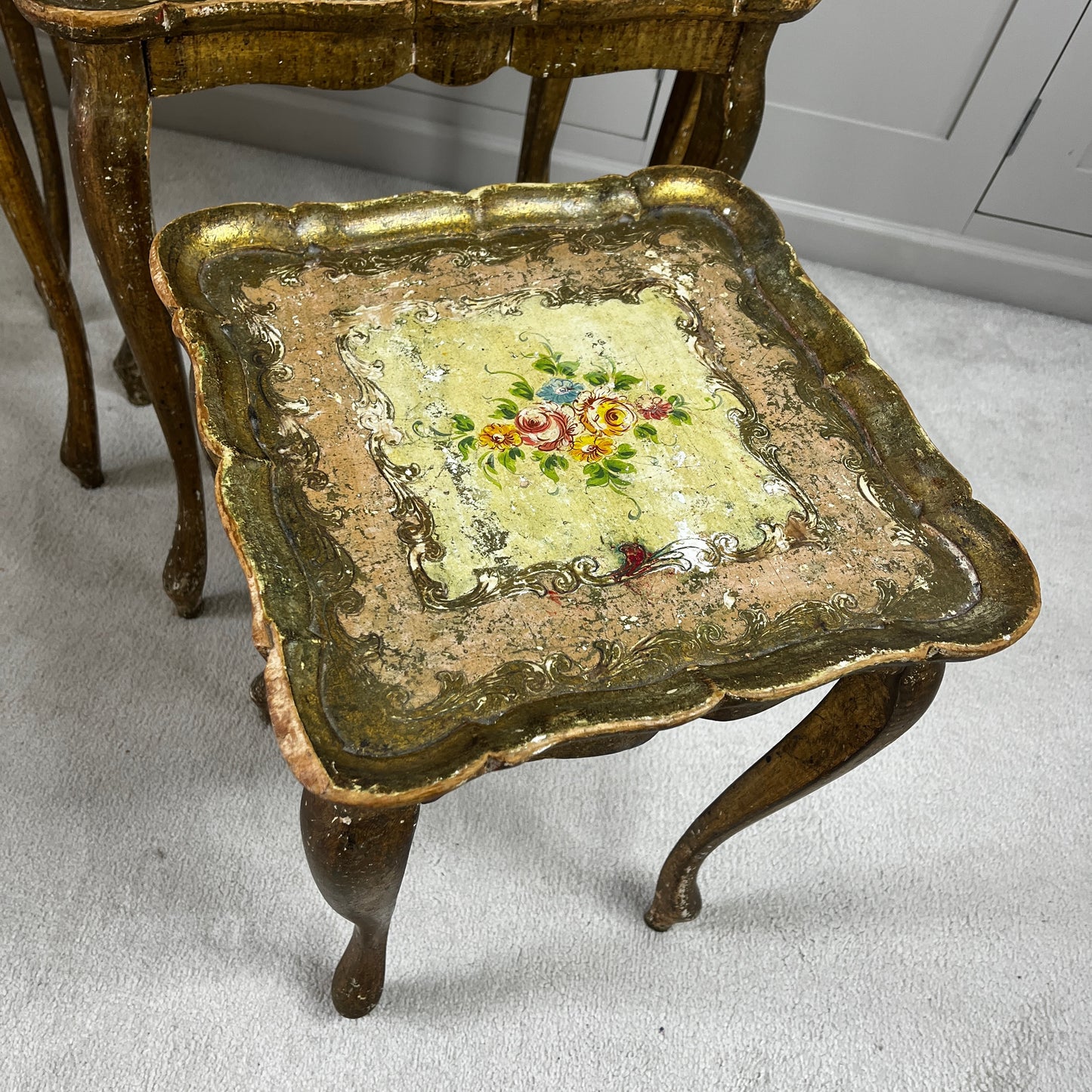 Vintage nest of three Florentine tables with ornate gilt detailing, shaped edges, and painted decorative surfaces in classic Italian style.