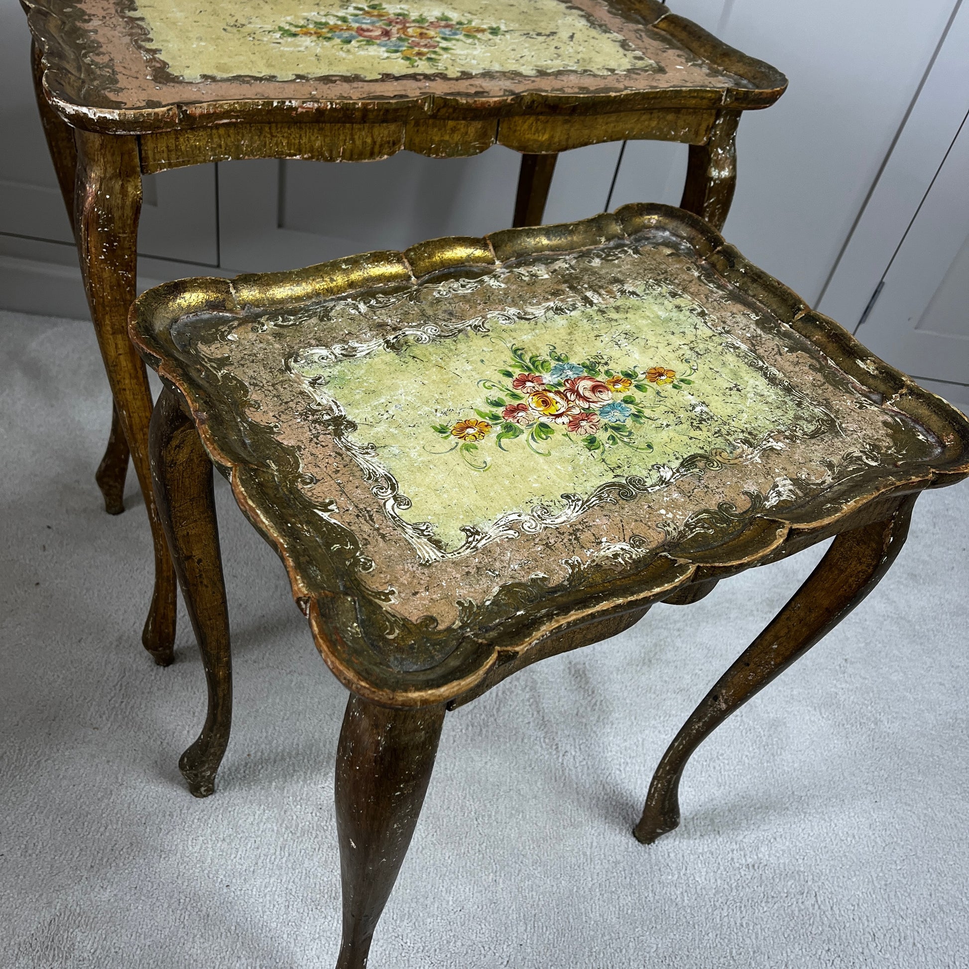 Vintage nest of three Florentine tables with ornate gilt detailing, shaped edges, and painted decorative surfaces in classic Italian style.