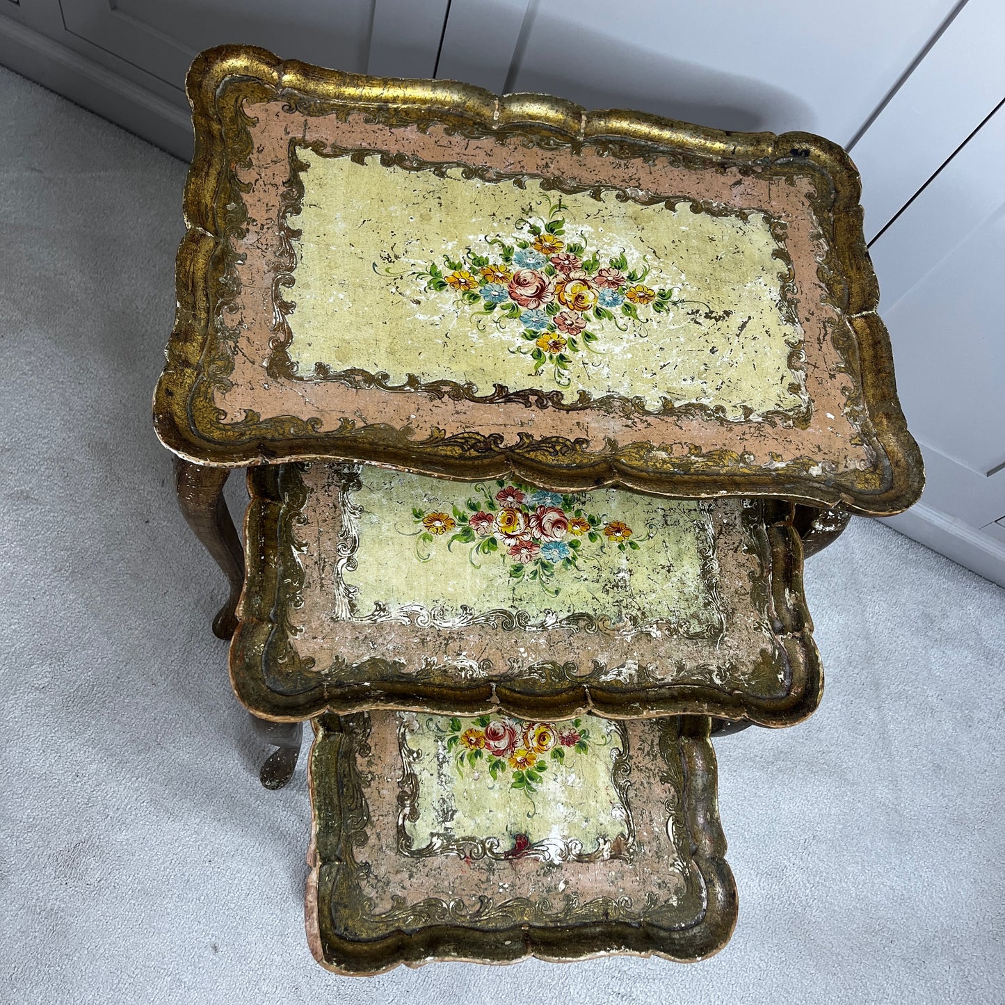 Vintage nest of three Florentine tables with ornate gilt detailing, shaped edges, and painted decorative surfaces in classic Italian style.