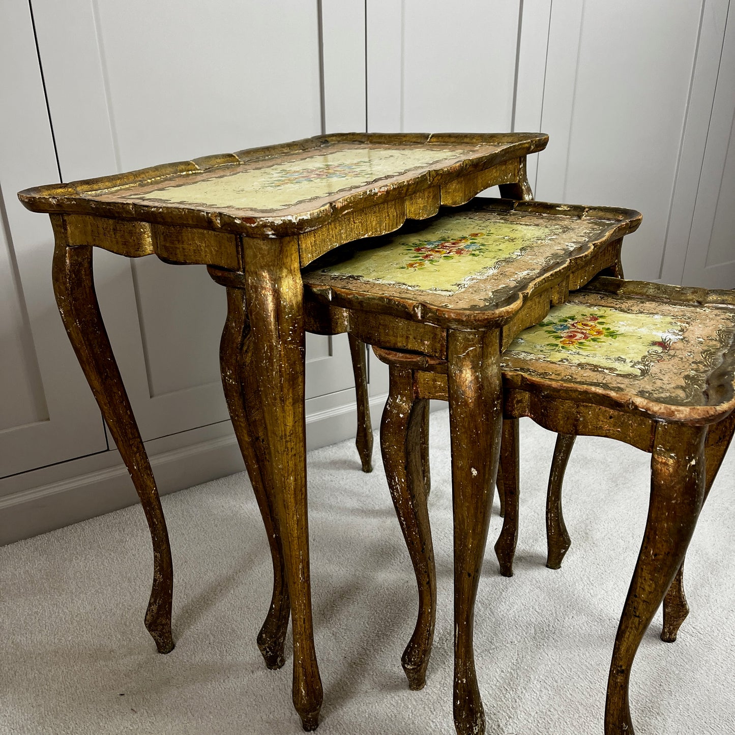 Vintage nest of three Florentine tables with ornate gilt detailing, shaped edges, and painted decorative surfaces in classic Italian style.
