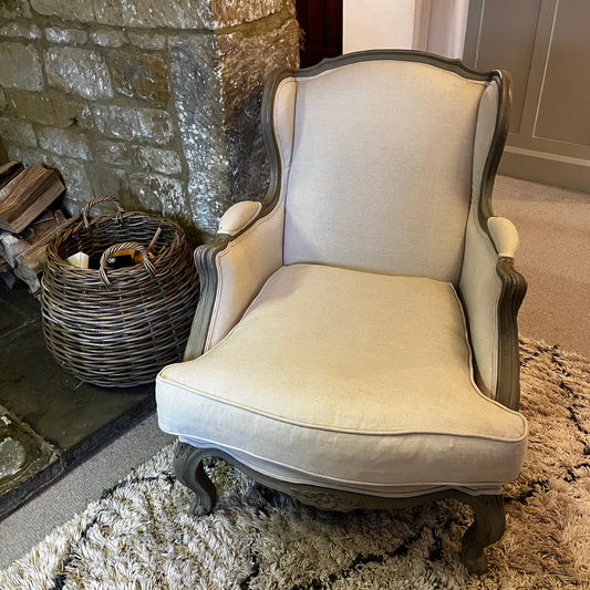 New French-style armchair with a carved wooden frame and linen upholstery, featuring a relaxed elegant silhouette and neutral fabric finish.
