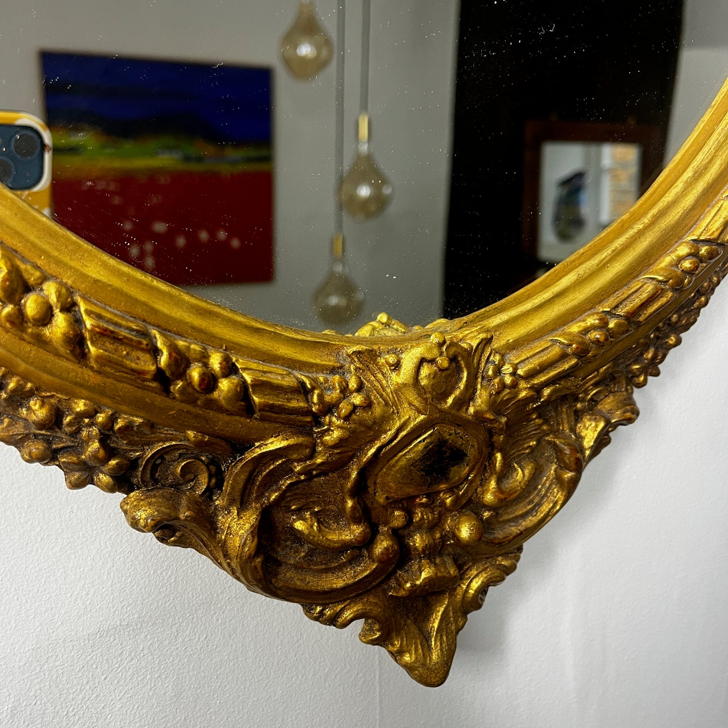 Oval gilded mirror with an ornate decorative frame featuring intricate detailing. The gold finish has a softly aged patina, giving the mirror an elegant, vintage appearance.