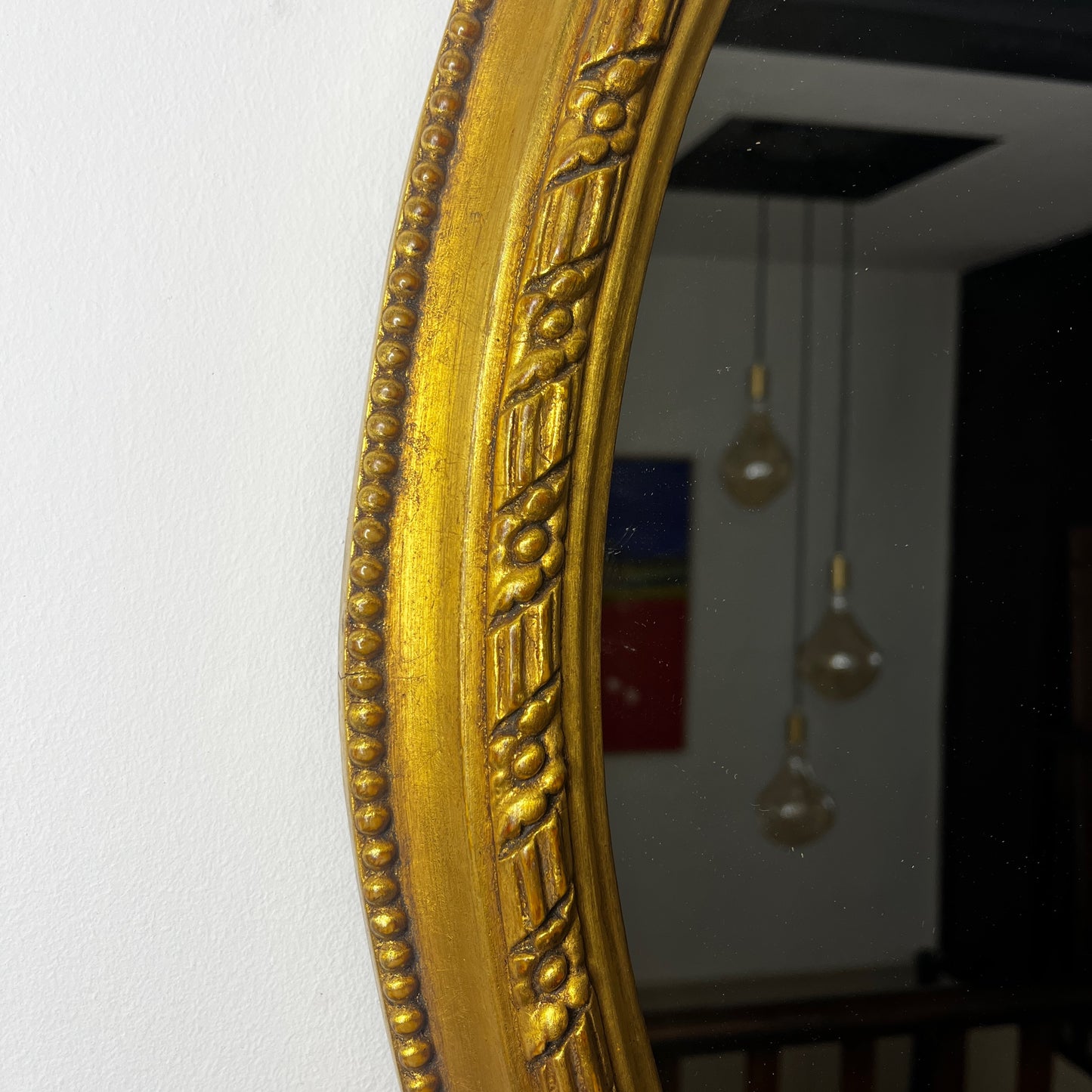 Oval gilded mirror with an ornate decorative frame featuring intricate detailing. The gold finish has a softly aged patina, giving the mirror an elegant, vintage appearance.