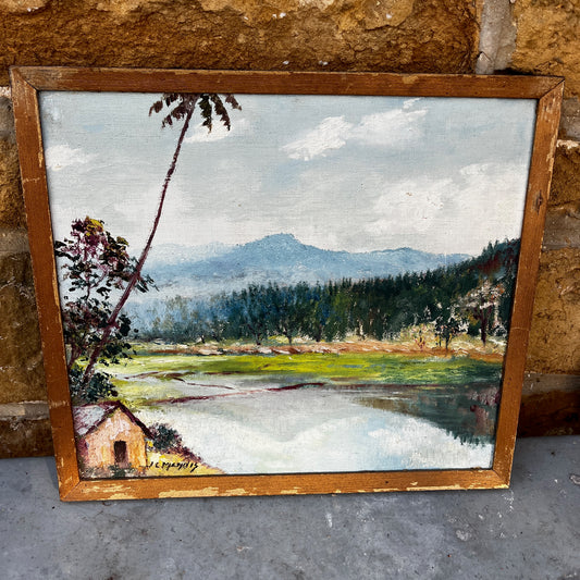 Framed vintage oil on board painting of a mountain lake scene, depicting tranquil water surrounded by rugged peaks and soft atmospheric light.

