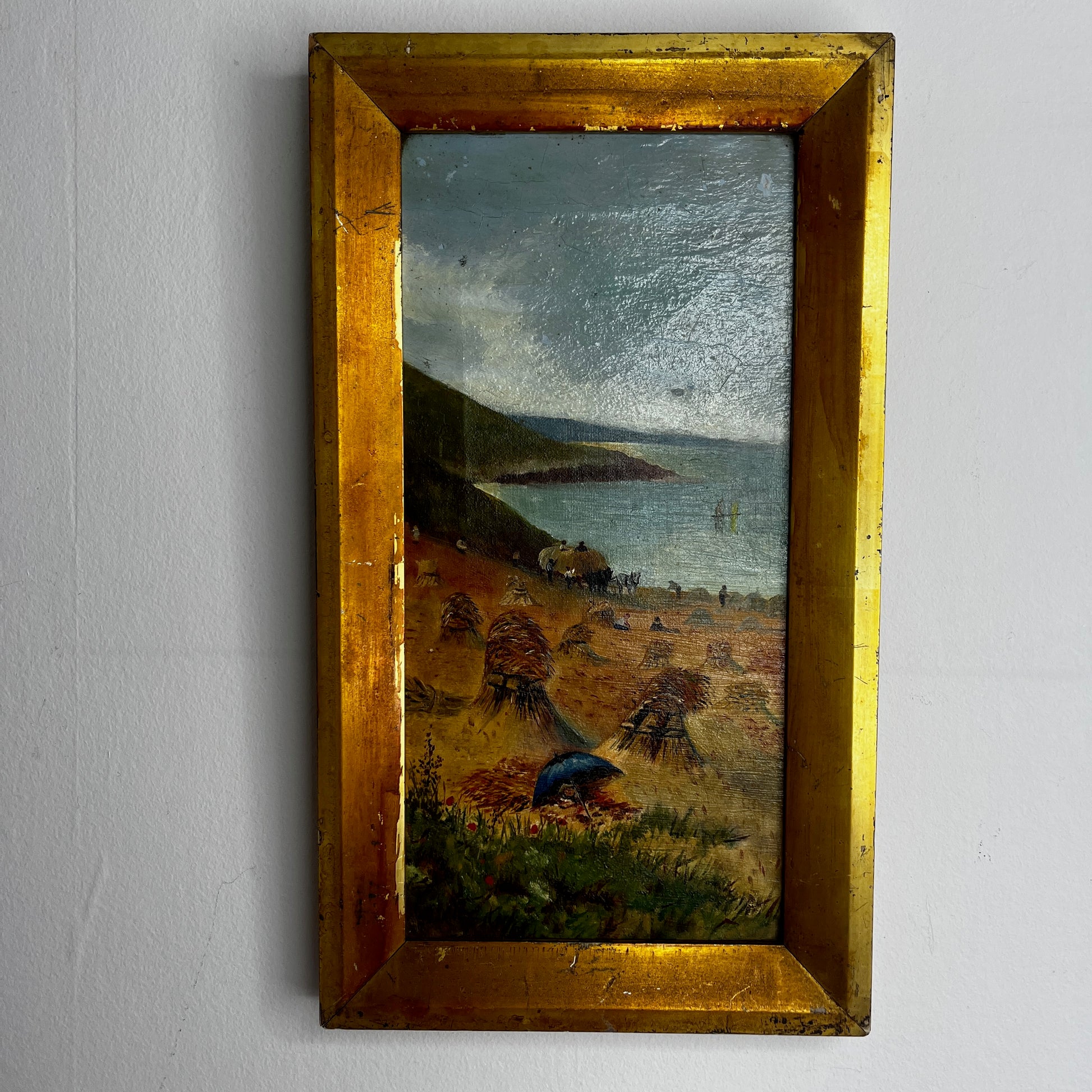 A vintage oil painting on canvas depicting a tranquil coastal scene with blue water, a sandy shoreline, and distant cliffs or headland beneath a softly painted sky. The atmospheric landscape is presented in an ornate gold-coloured frame, adding a classic, elegant touch to the artwork