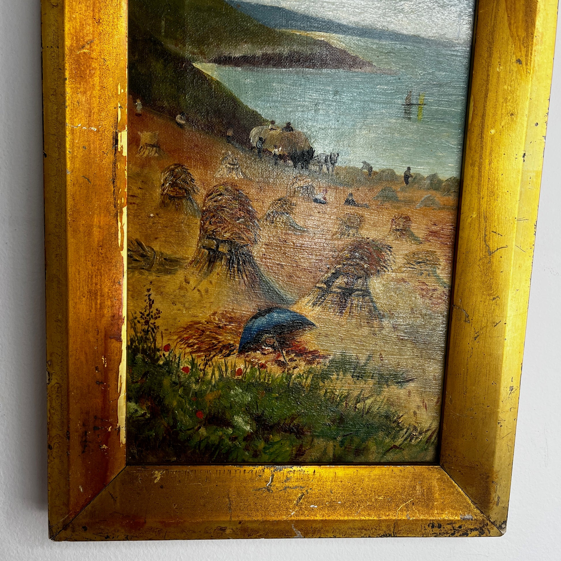 A vintage oil painting on canvas depicting a tranquil coastal scene with blue water, a sandy shoreline, and distant cliffs or headland beneath a softly painted sky. The atmospheric landscape is presented in an ornate gold-coloured frame, adding a classic, elegant touch to the artwork