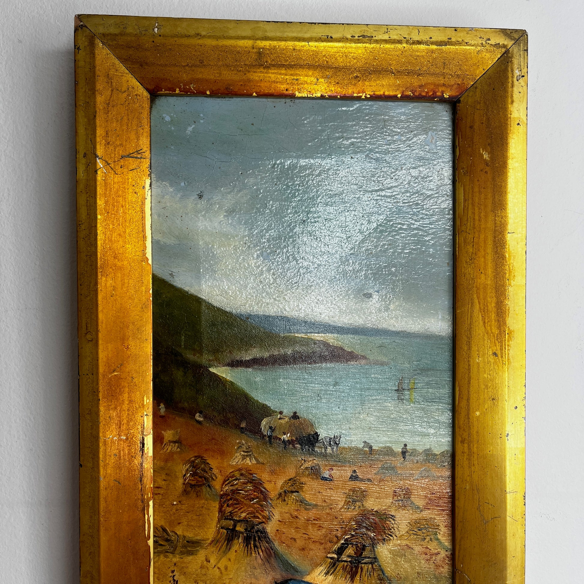 A vintage oil painting on canvas depicting a tranquil coastal scene with blue water, a sandy shoreline, and distant cliffs or headland beneath a softly painted sky. The atmospheric landscape is presented in an ornate gold-coloured frame, adding a classic, elegant touch to the artwork