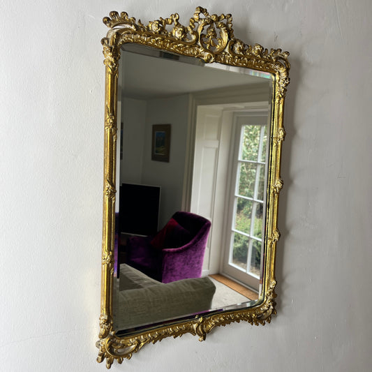 A vintage Rococo-style gilded beveled mirror with an ornate, intricately carved frame featuring scrolling foliage, shells, and asymmetrical rocaille motifs, finished in a rich gold leaf patina.