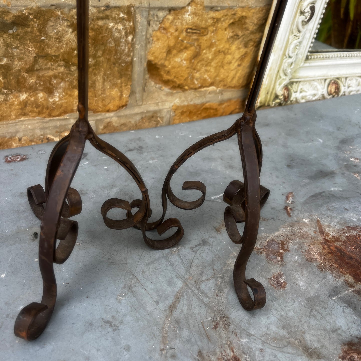 A pair of rustic black metal French-style candle holders with an aged, weathered finish. Each features an elegant turned stem, decorative detailing, and a sturdy tripod base