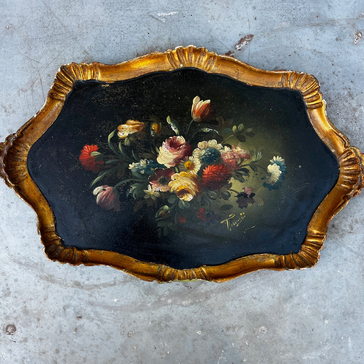 An antique oval tray featuring a painted floral bouquet in the center and a scalloped gold frame