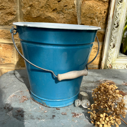 Vintage-style blue metal bucket with white enamel interior and wooden grip handle, placed on a rustic surface