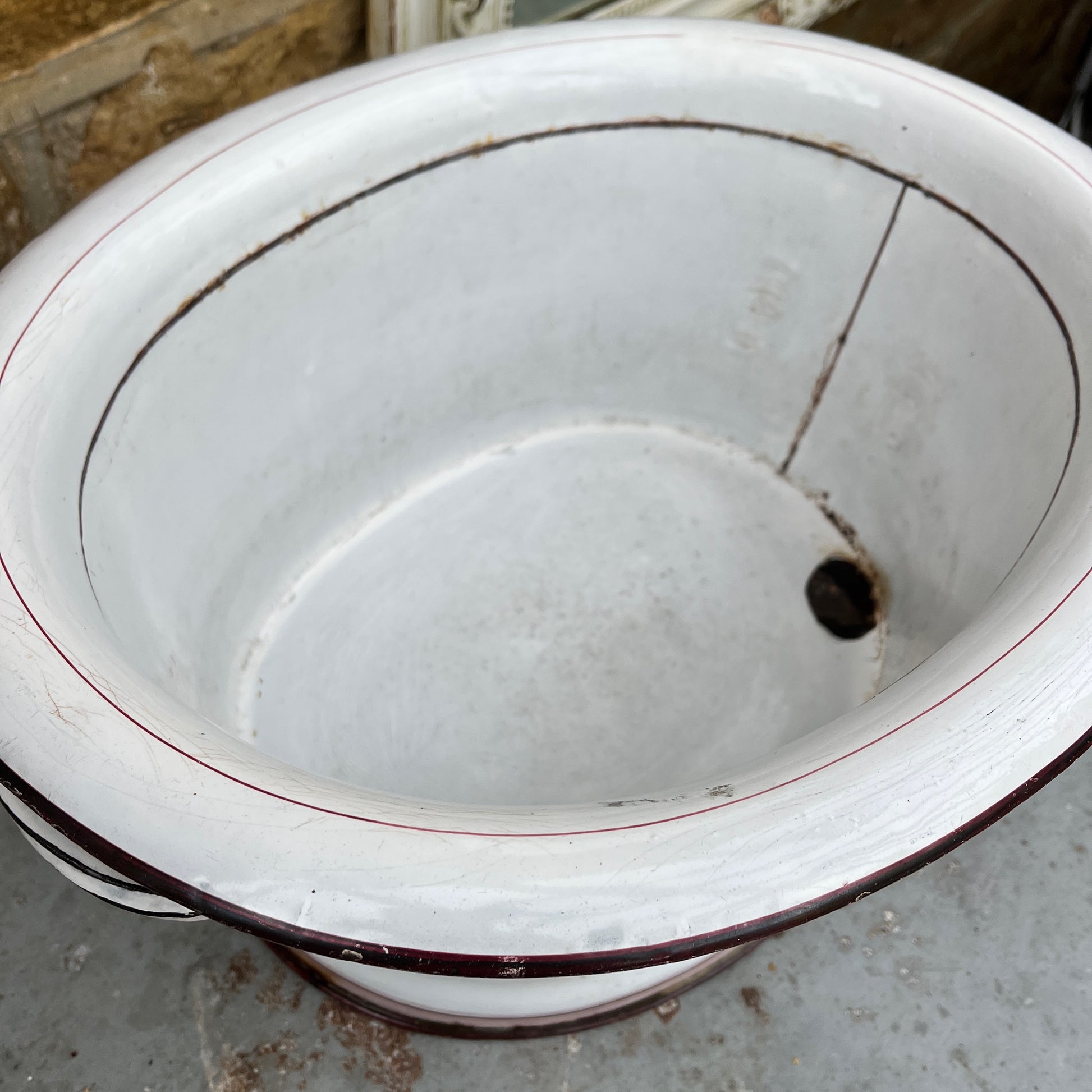 A large vintage French white enamel wash bowl, circa early 20th century, featuring a wide, deep basin. The bowl is adorned with delicate pink stripes,  with a smooth white enamel finish showing minor chips and rust spots, characteristic of its aged, rustic charm.
