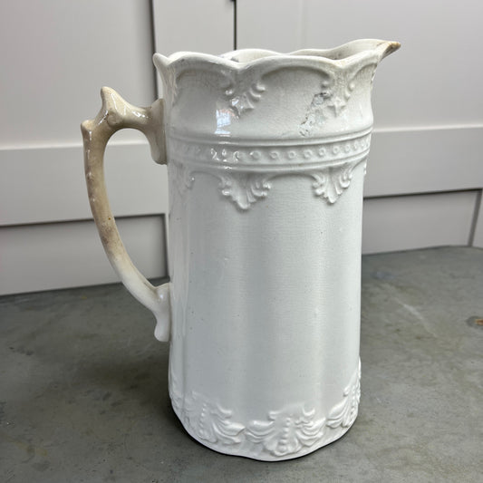White ceramic pitcher with decorative patterns on a gray surface.