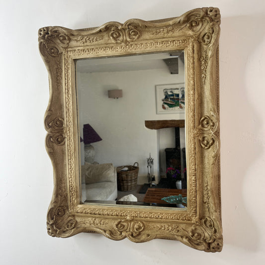 A vintage beveled rectangular mirror with a polished glass surface, framed by a weathered wooden decorative border in a warm, aged finish