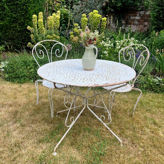 Vintage outdoor metal table and chairs with a vase of flowers in a garden setting