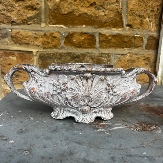 An antique Rococo-style cast iron jardiniere featuring an ornate decorative design with scrolling details, curved handles, and an aged, weathered finish