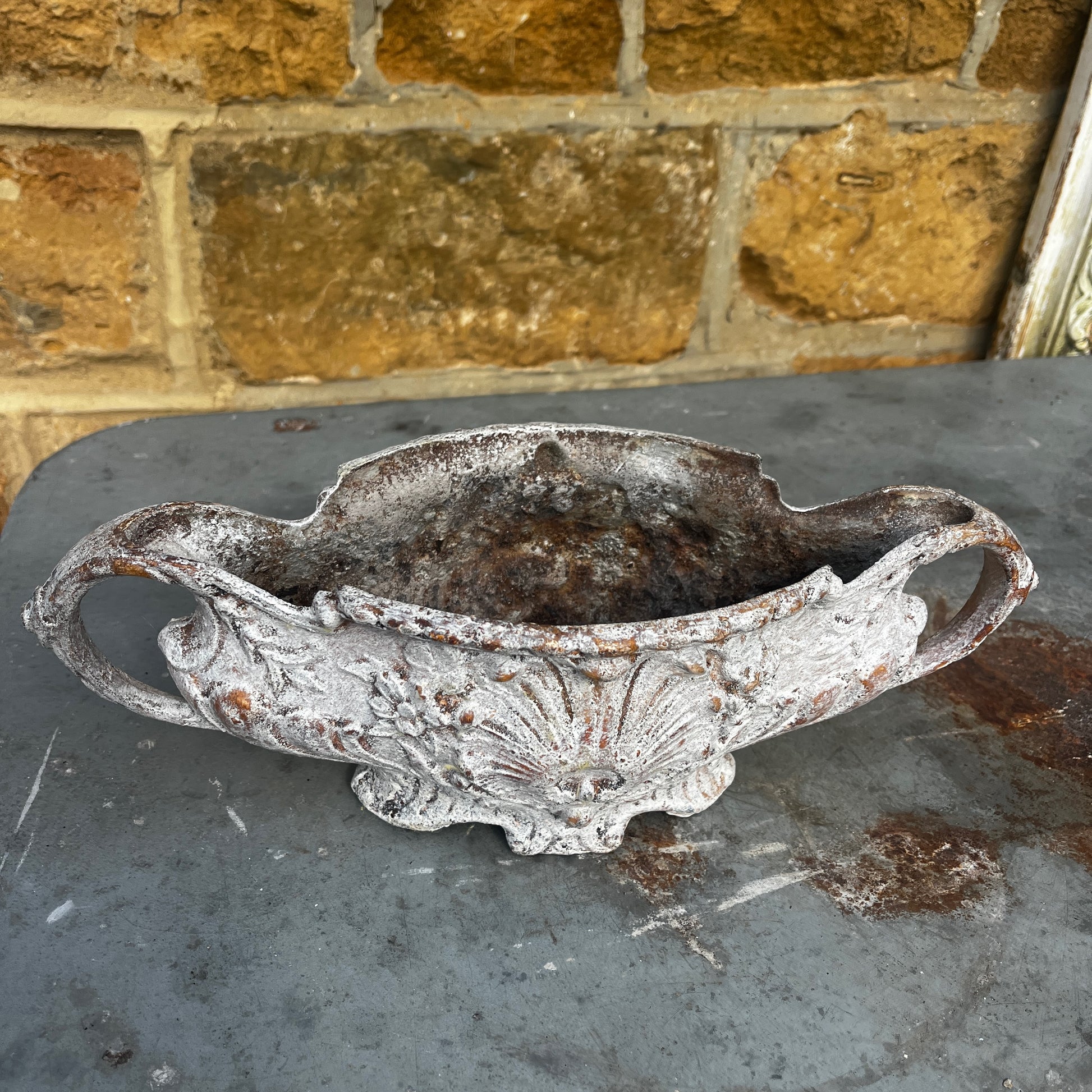 An antique Rococo-style cast iron jardiniere featuring an ornate decorative design with scrolling details, curved handles, and an aged, weathered finish