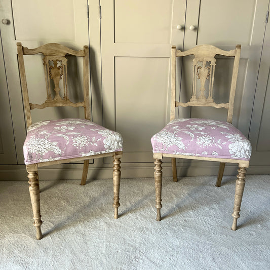 A pair of vintage occasional chairs featuring delicate wooden backs with carved details and pink upholstered seats, blending elegant craftsmanship with a soft, vintage charm.
