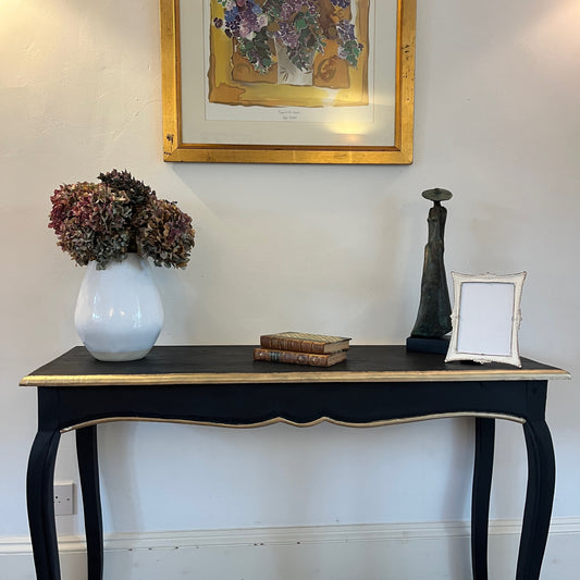 A wooden vintage console table with a black finish, accented by elegant gold detailing along the edges.  Presenting a sophisticated vintage design perfect for a hallway or living space.