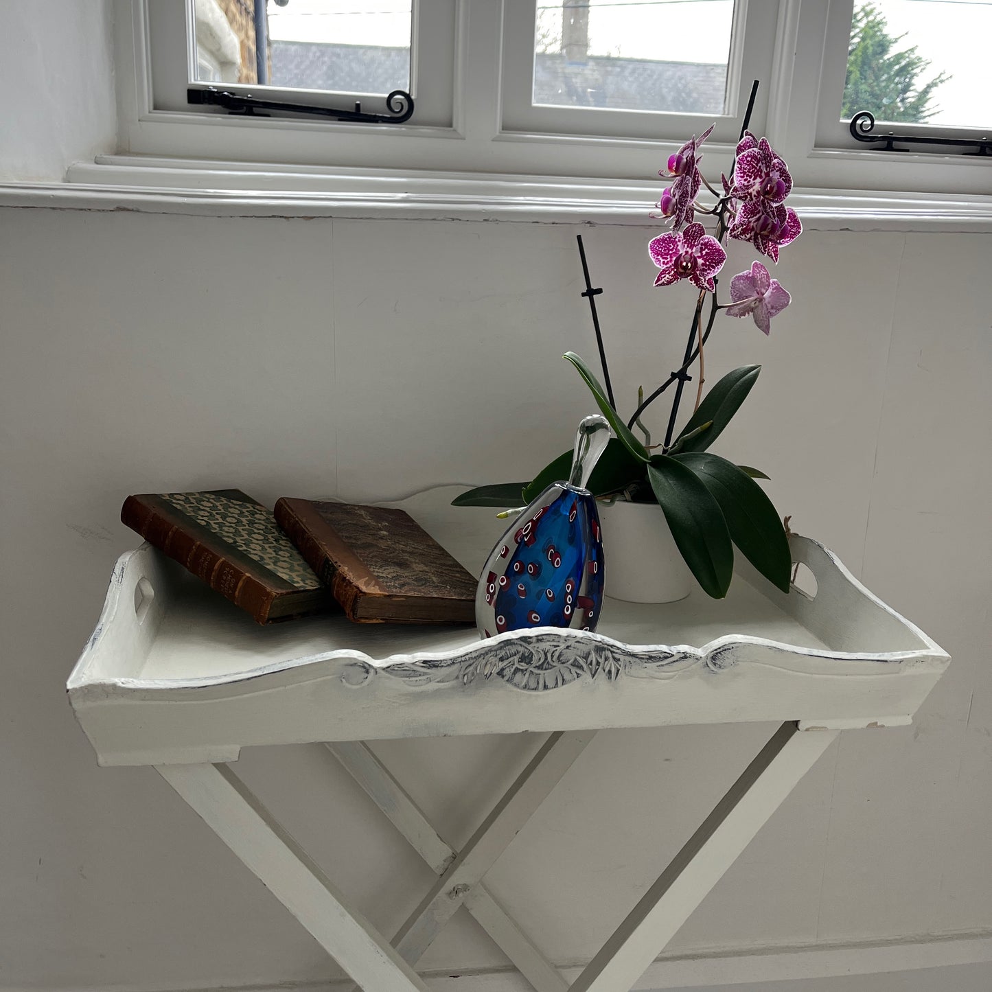 A white butler‚Äôs tray, which has been painted and distressed, featuring a rectangular shape with raised edges and two sturdy handles on either side, designed for versatile serving or display.