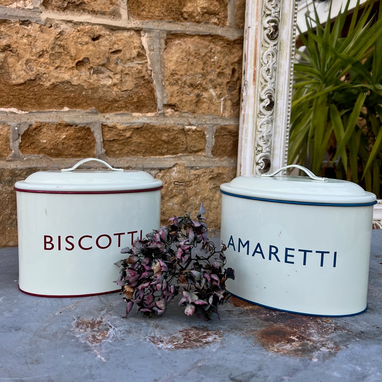 Two enamel biscuit tins with the words Amaretti and Biscotti on the front