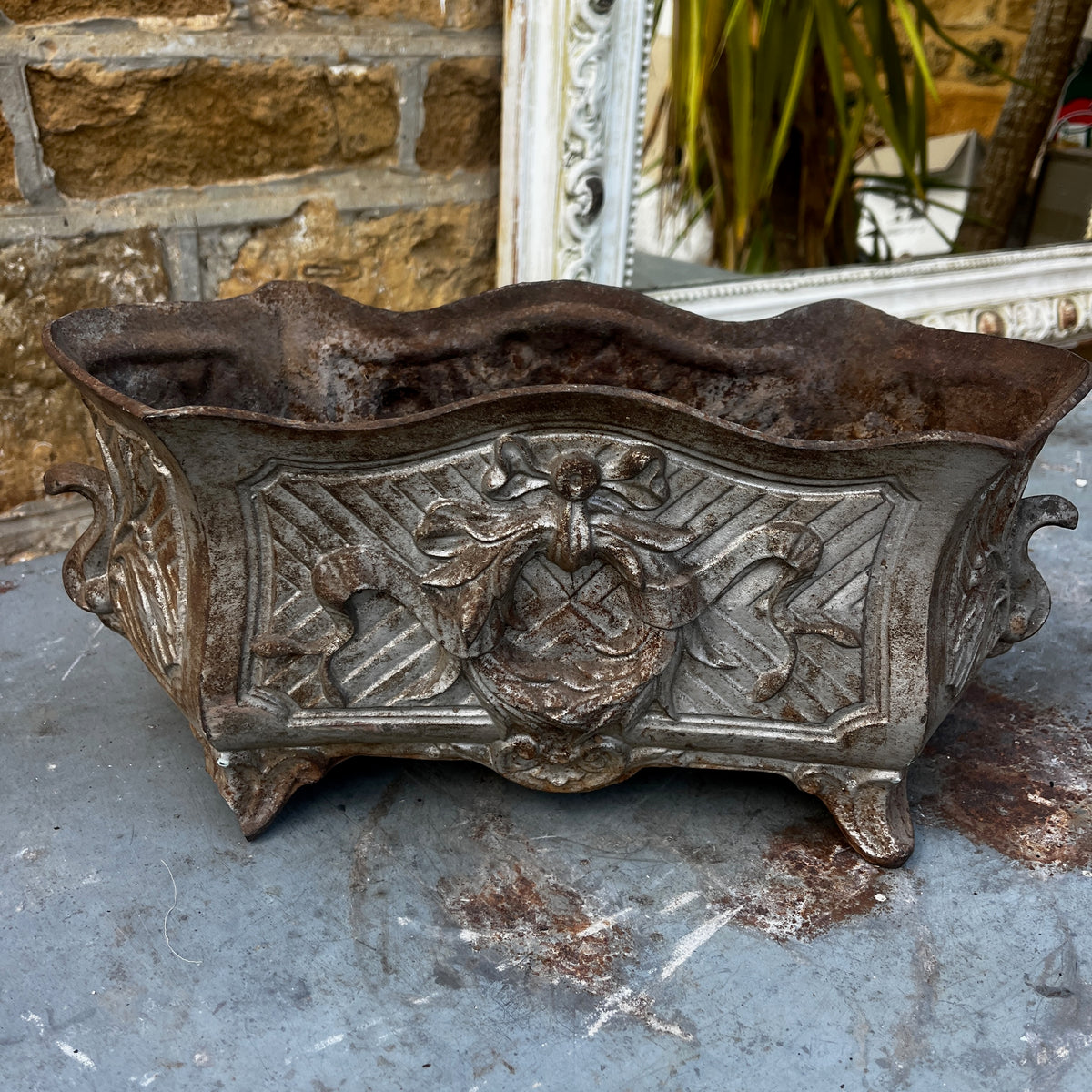An ornate vintage cast iron planter with a distressed silver and brown patina, featuring a central crest and scrollwork.