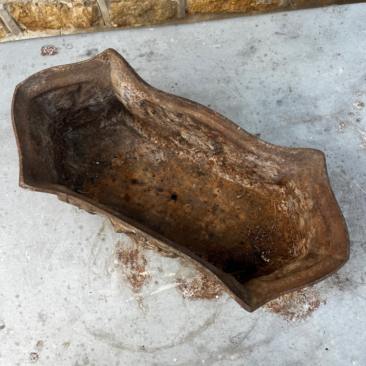 An ornate vintage cast iron planter with a distressed silver and brown patina, featuring a central crest and scrollwork.