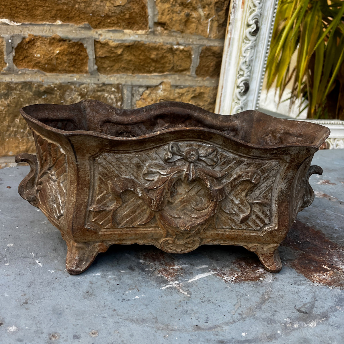 An ornate vintage cast iron planter with a distressed silver and brown patina, featuring a central crest and scrollwork.
